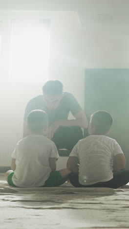 el entrenador habla con los niños en el descanso en el club de artes marciales. los niños pequeños descansan con el joven instructor sentado en la alfombra del suelo en el gimnasio en cámara lenta. lección de lucha