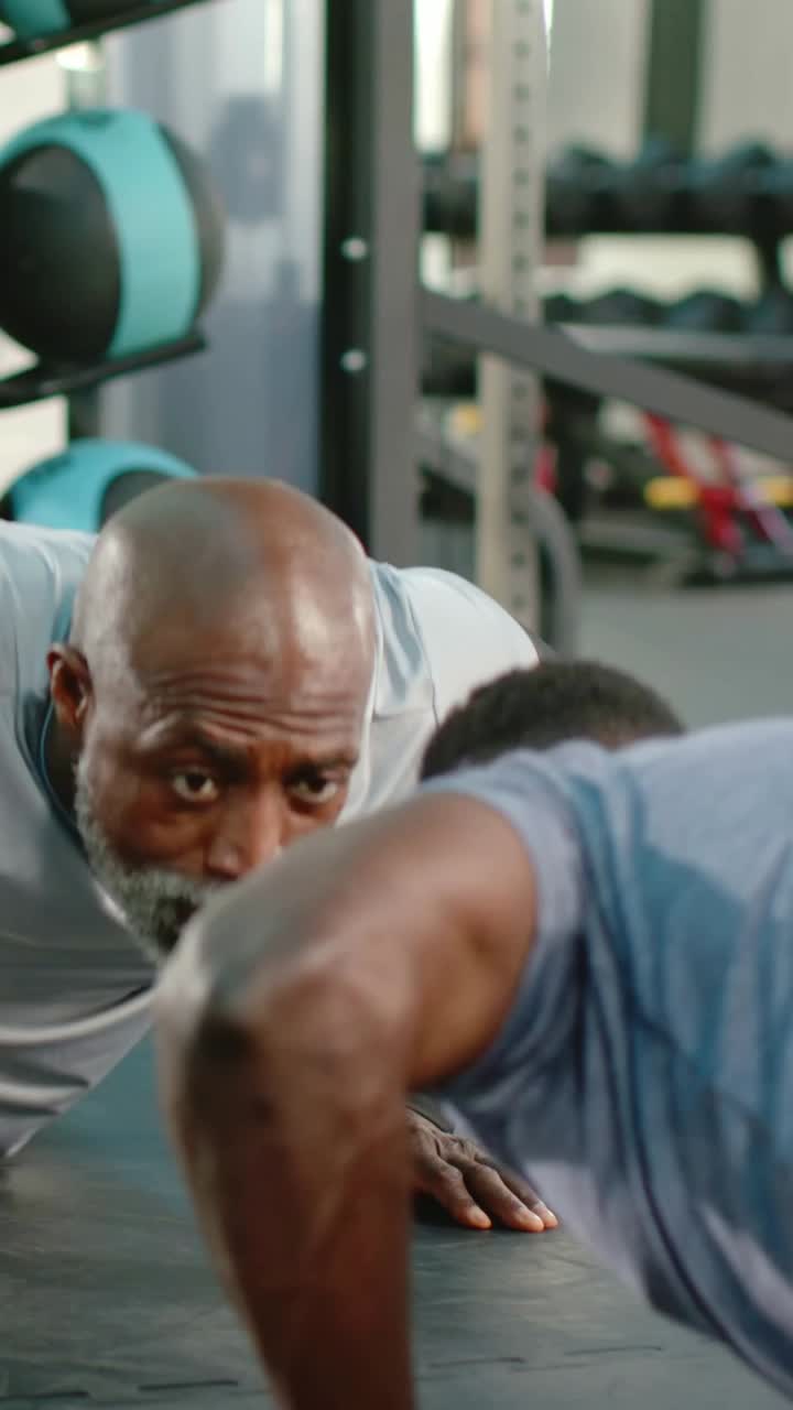 Vertical video: Coaching trainer cueing client doing pushups for form on gym mat, in black sleeves