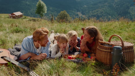 Friendly-family-enjoy-picnic-on-grass-mountain-hill.-Happy-people-lying-blanket.