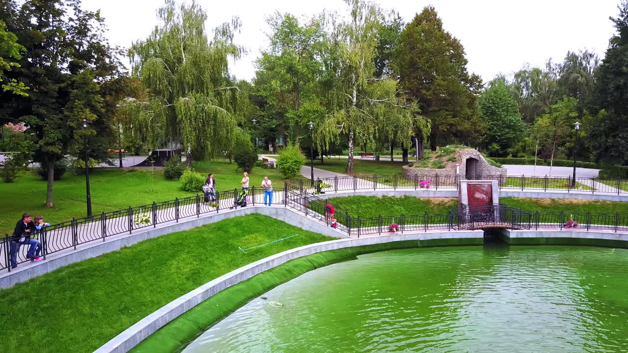 People spending time in the beautiful city park. Visitors enjoying the view of fountains on the pond.