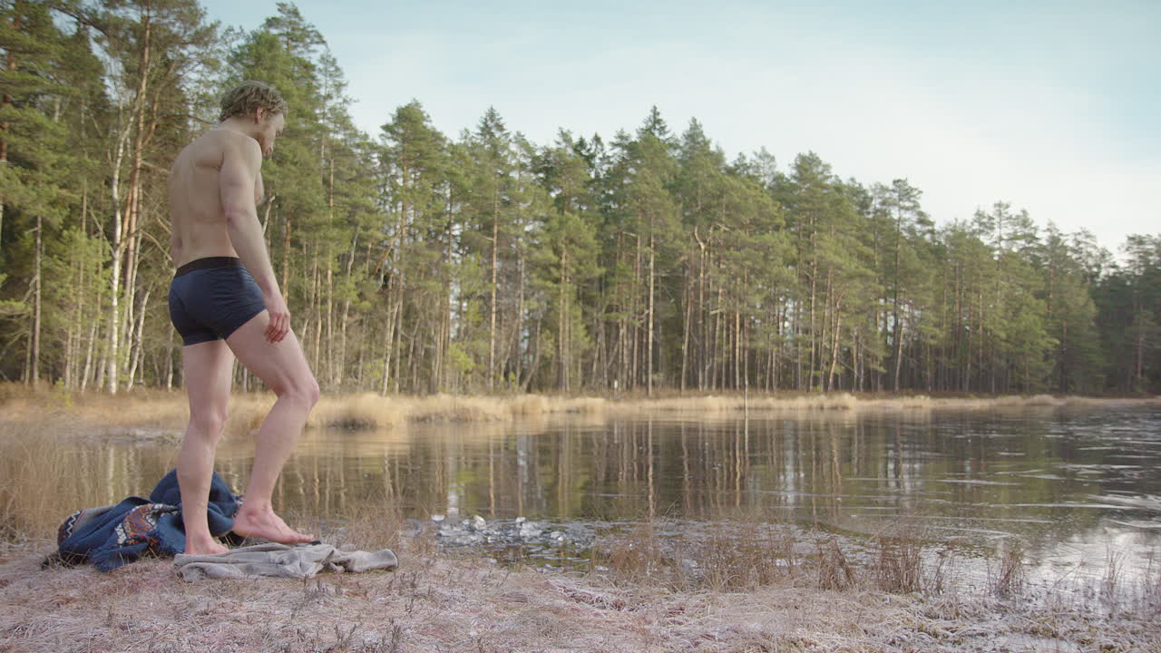 acercar - un bañista de hielo muscular en forma se quita el poncho y se prepara para entrar en el lago congelado