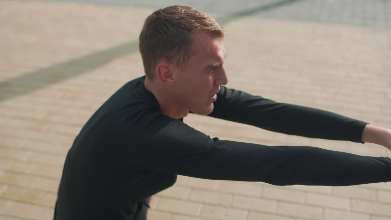 white man performing controlled squat in plaza arms extended steady descent sunlit paving focused trainer demonstrating bodyweight technique athlete testing balance core stability slow deliberate