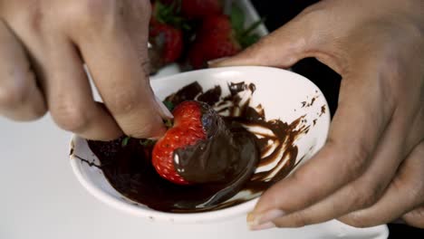 spinning a strawberry into melted chocolate to make chocolate covered strawberry vegan valentines day