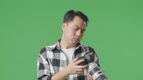 카메라에서 사진을 보고 머리를 흔들고 있는 아시아 사진작가, 스튜디오의 녹색 스크린 배경에서 결과에 불만을 품고 있다.