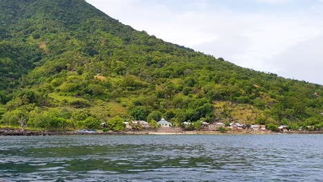 Small-community-of-houses-nestled-amongst-trees-on-shoreline-of-tropical-island-on-Alor-Island-in-Lesser-Sunda-Islands-of-East-Nusa-Tenggara,-Indonesia