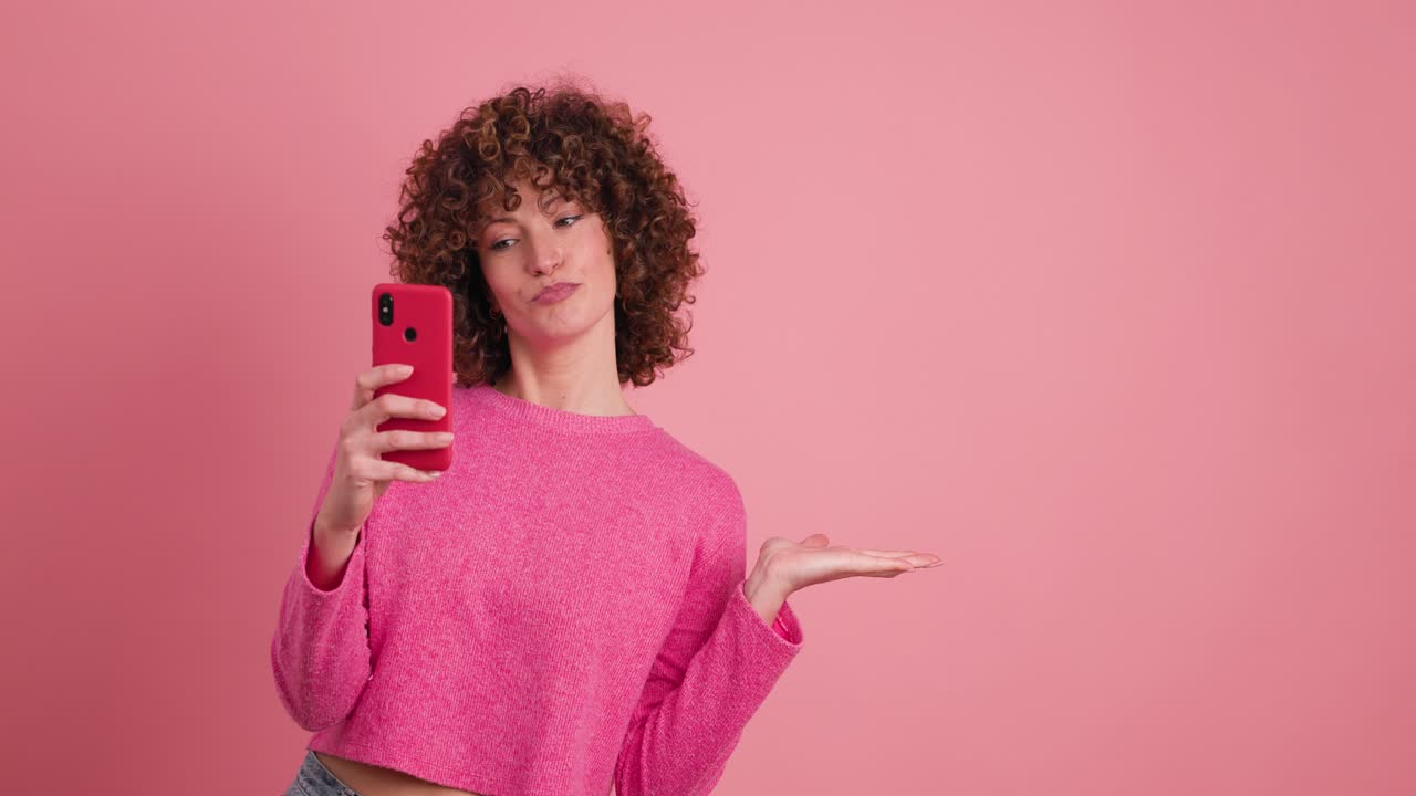 Mujer feliz usando teléfono móvil señalando en estudio rosa