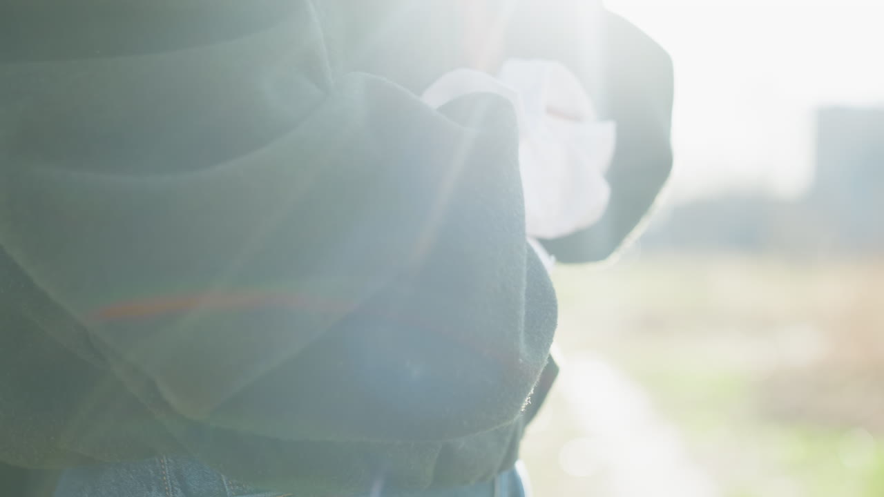 Close up adult woman adjusting sleeve of dark jacket outdoors, white shirt cuff showing, casual denim jeans visible, natural daylight, candid gesture capturing relaxed lifestyle moment