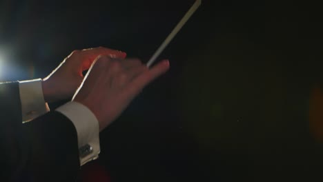 moving hands of an orchestra conductor directing musicians with movement of baton on black background with lights. conducting, directing classical musical performance with visible gestures. close up