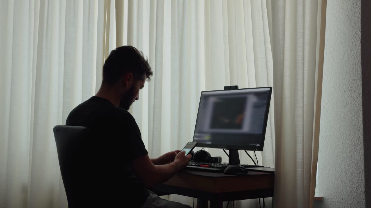 joven sentado frente a la computadora trabajando y editando videos dentro de una habitación de una casa