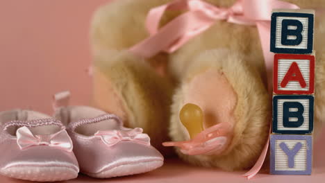 pink soother falling besides baby shoes blocks and teddy bear