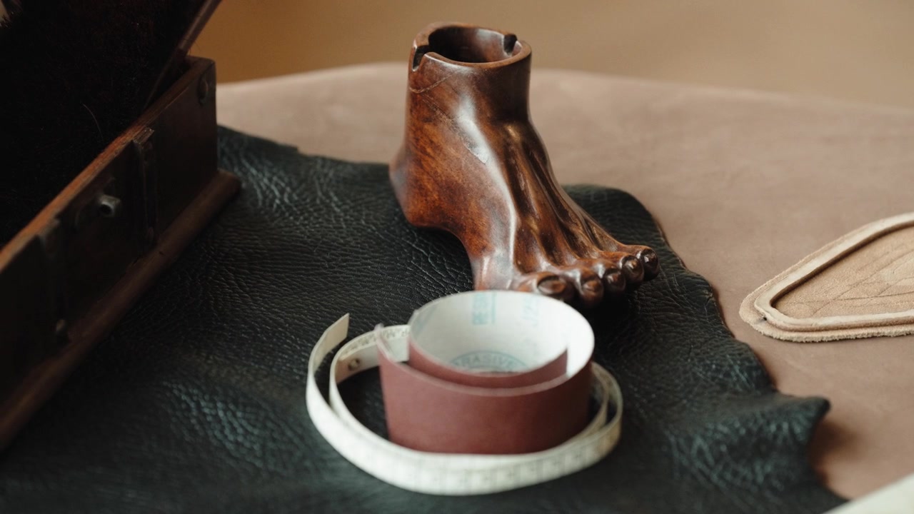Wooden foot sculpture beside a coiled tape measure and sandpaper on black leather