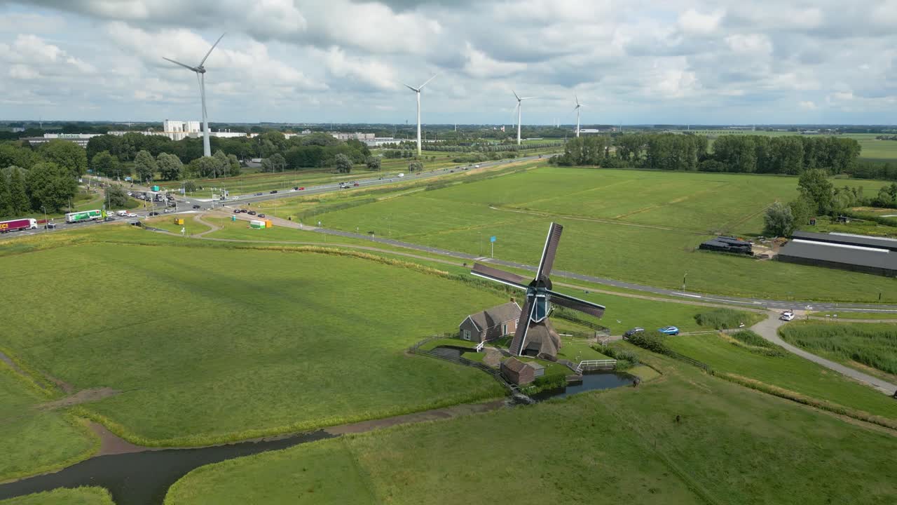 Drone footage of traditional windmill surrounded by wind turbines in rural green farmland landscape