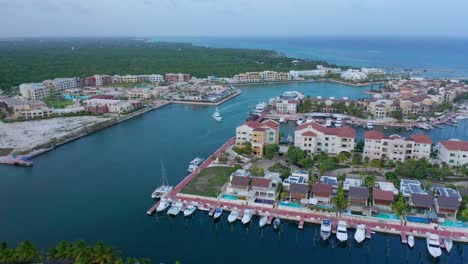 Toma-Panorámica-Del-Puerto-Deportivo-De-Cap-Cana,-Hermosos-Edificios-De-Agua-Azul,-Yate-Blanco-Haciendo-Su-Entrada