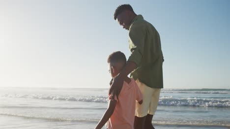 feliz padre afroamericano caminando con su hijo en una playa soleada