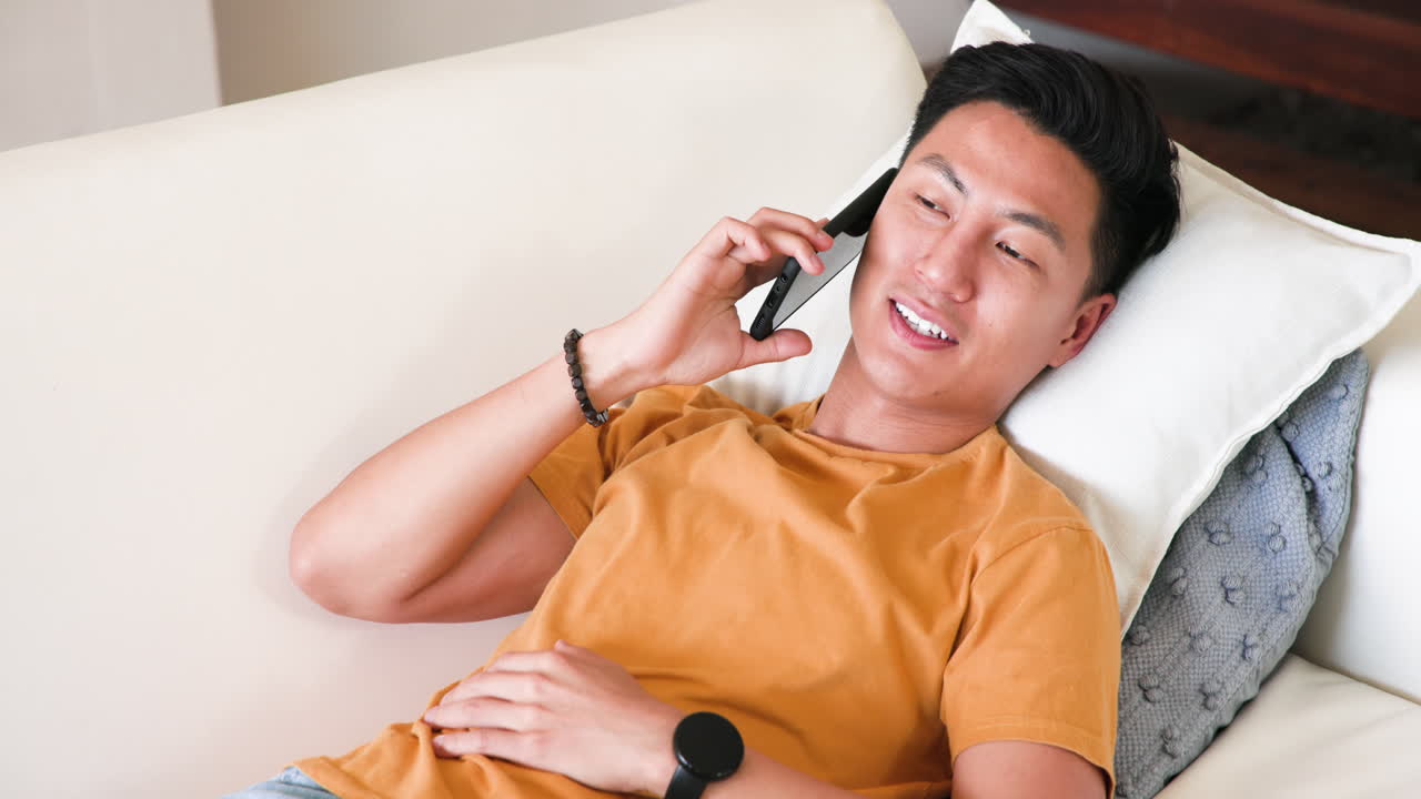 Relaxing on couch, Asian man browsing smartphone at home, enjoying leisure time