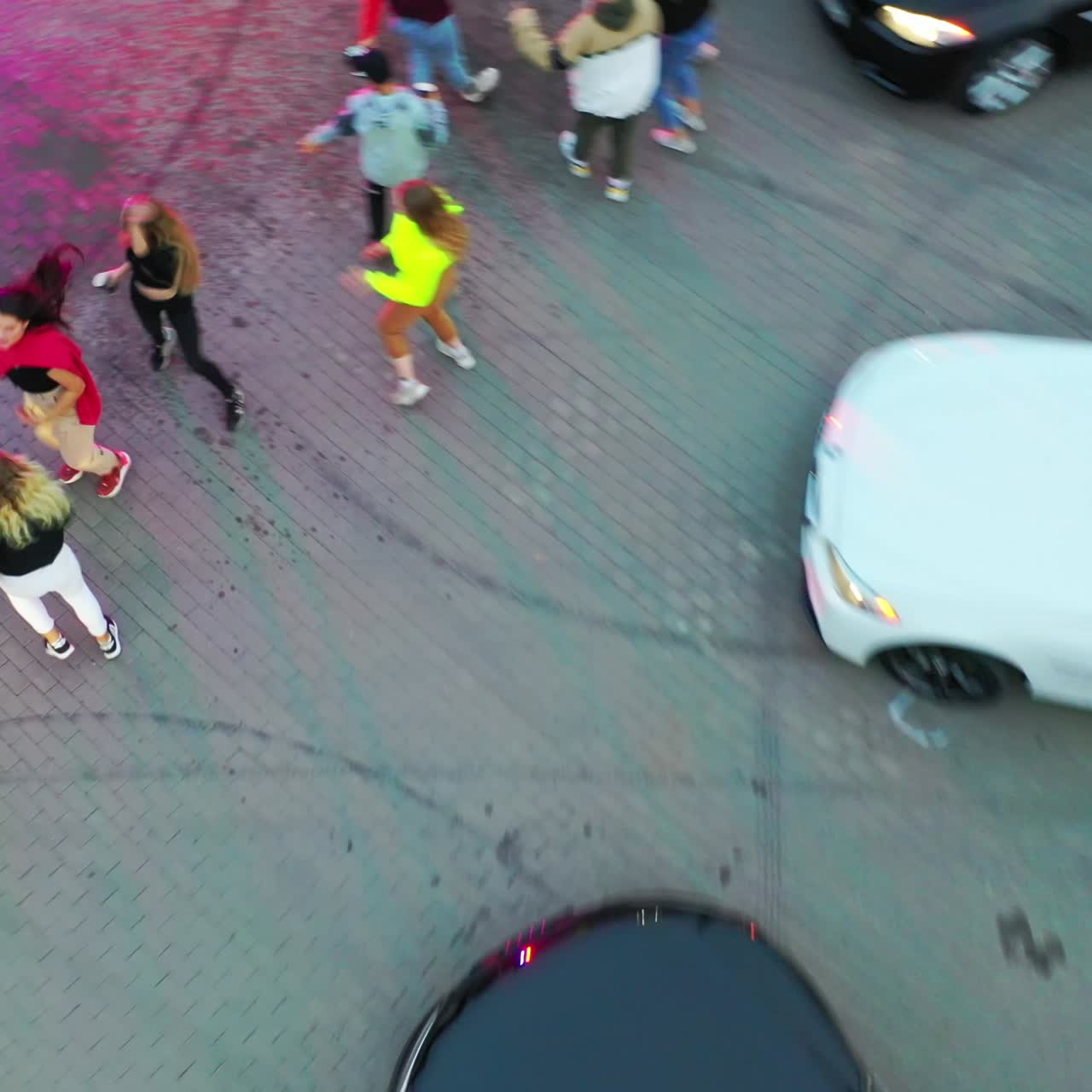 Girl in a black hoodie dancing surrounded by her friends also moving. Cars for drift around the people. Top view