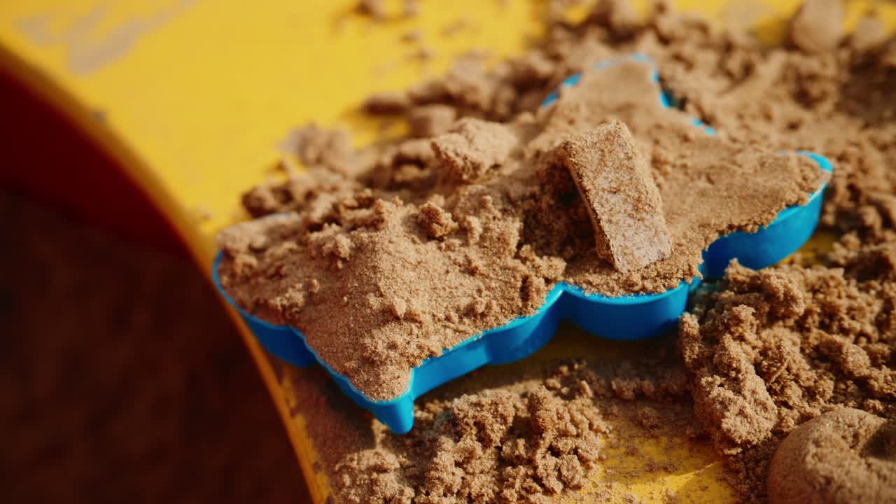 A Child's Hands Creating Sand Shapes in a Colorful Sandbox with a Blue Mold, Encouraging Imagination and Playful Exploration with Natural Materials