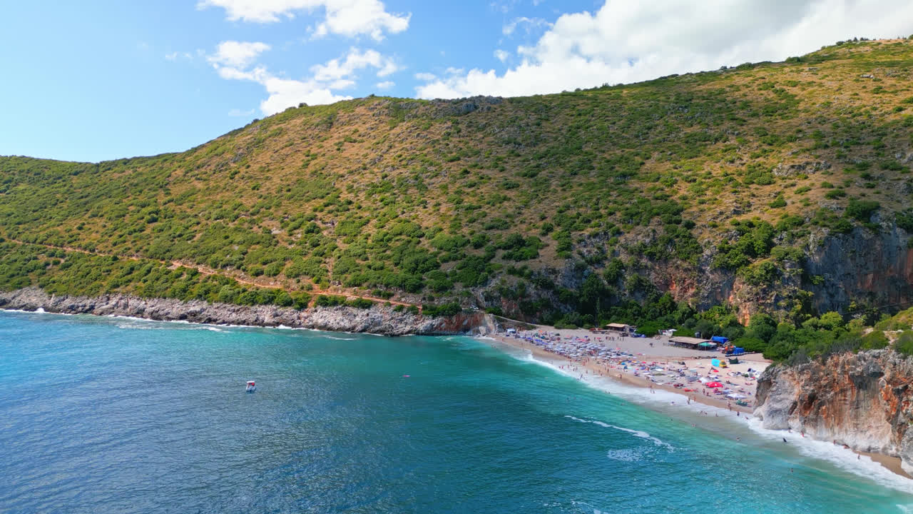 Aerial drone shot flying over Gjipe beach alongside Ionian Sea with impressive canyon and mountains in the background on a cloudy day