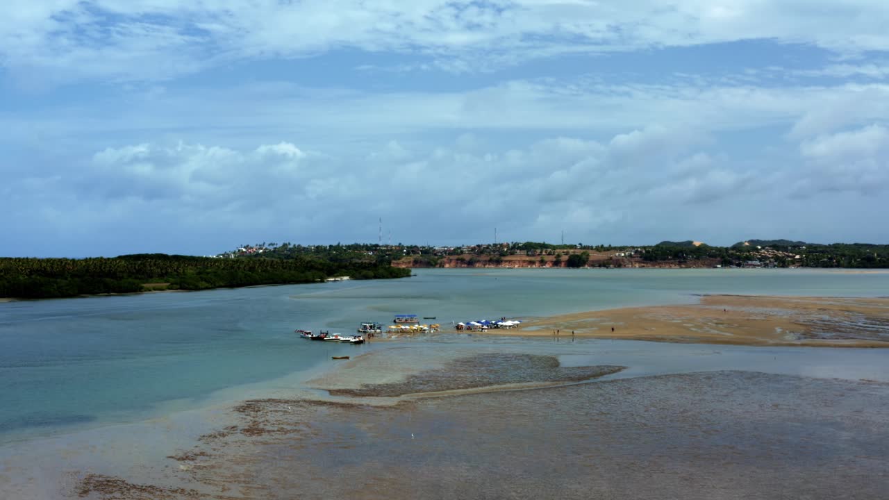 Rising tilting down aerial drone shot of a large natural sand bar colorful umbrellas in the tropical Guara&iacute;ras Lagoon in the touristic beach town of Tibau do Sul, Brazil in Rio Grande do Norte