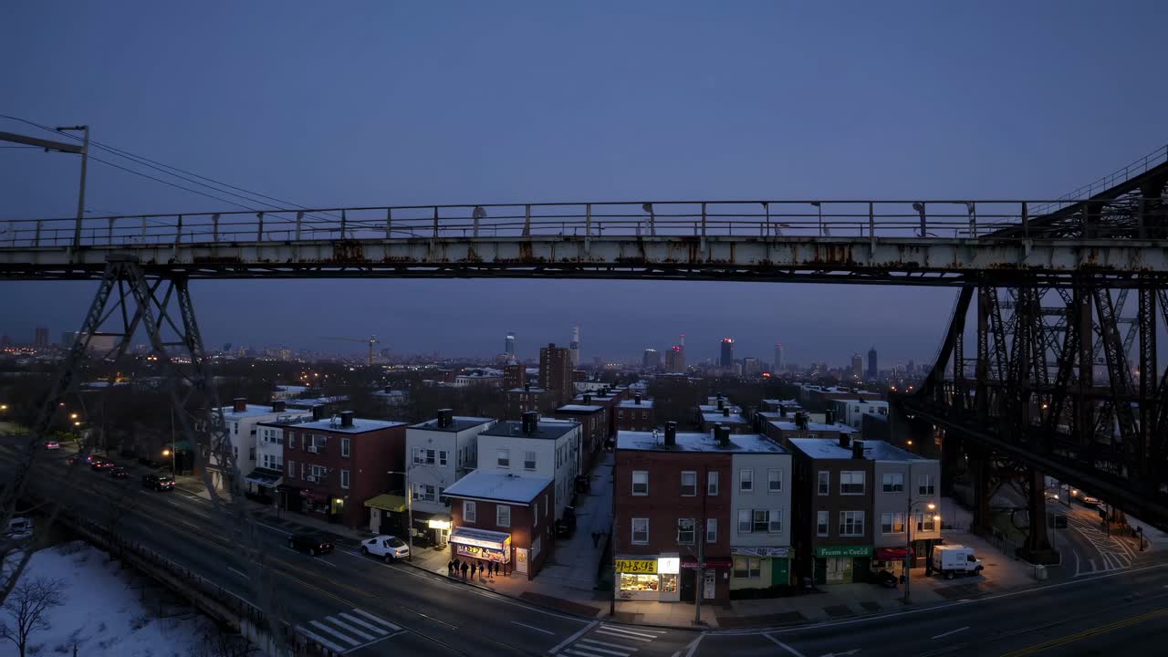 Aerial video view of an urban bridge at dusk, capturing city lights and rooftops below