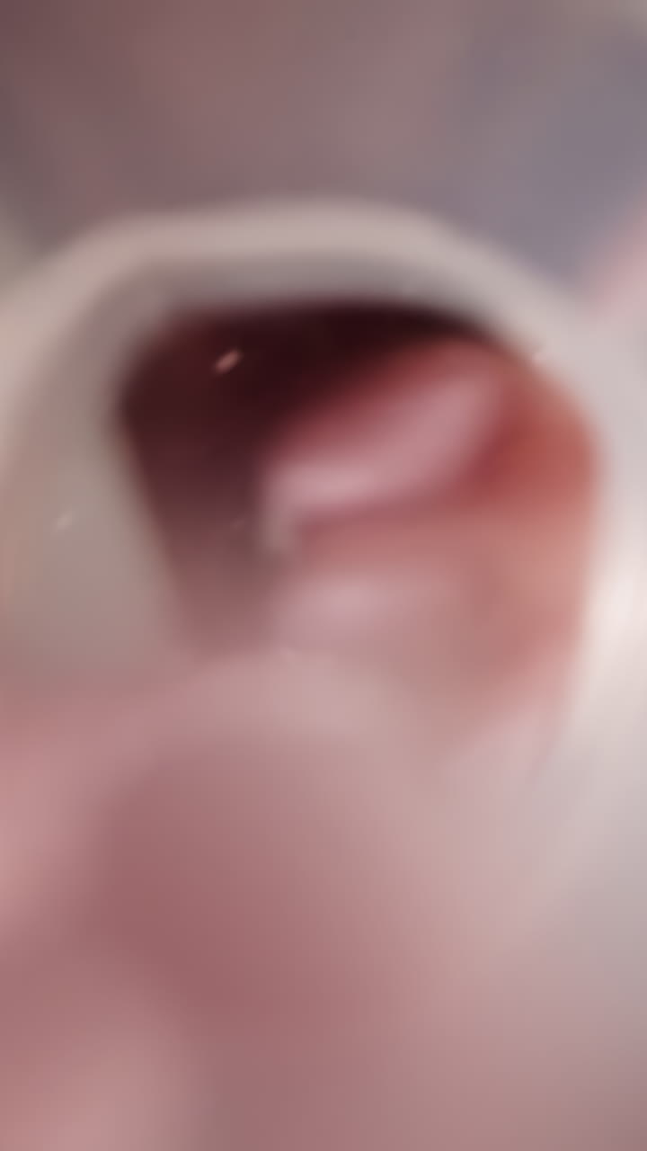 Female hand pours bright colored balls from plastic tube into clear water. Woman prepares sweet drink adding soluble candies. Preparing beverage in kitchen at home macro