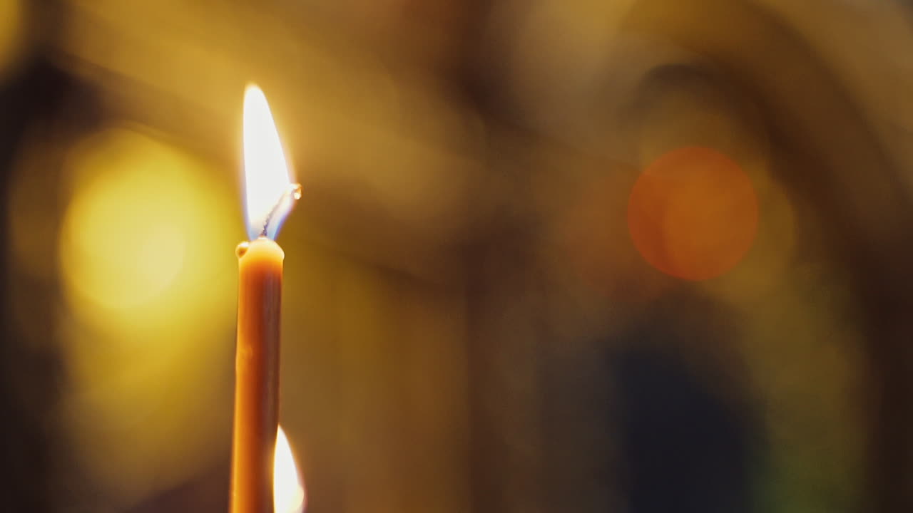 One candle is glowing brightly in church. Golden light of candle flame. Burning candle is the symbol of spirituality. Close-up.