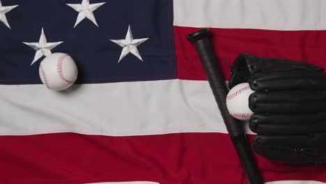 overhead baseball still life with bat and catchers mitt on american flag with ball rolling into frame 2