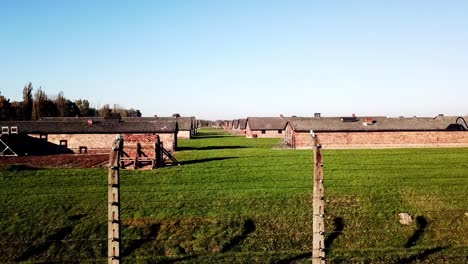 Drone-Subiendo-Detrás-De-La-Cerca-Y-Tirando-Hacia-Atrás-Del-Cuartel-En-Auswitz-Birkenau,-Polonia,-Europa