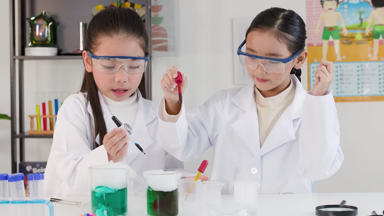 保護メガネを着用したアジアの女子生徒たちが、教室で化学実験のためにピペットを使用しています。