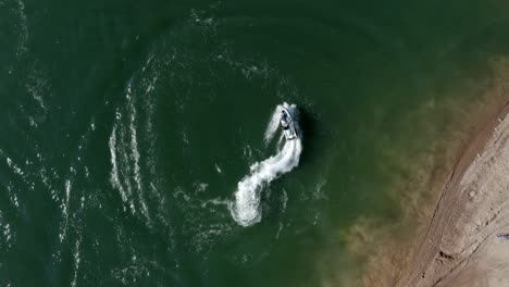 Person-on-a-jet-ski-turning-tight-circles-near-the-beach---bird's-eye-aerial-view