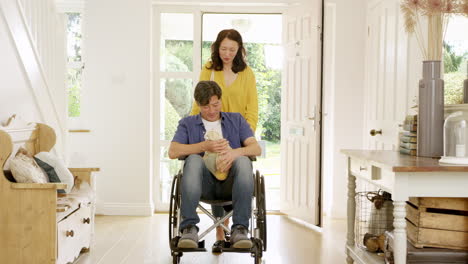 mature asian woman pushing husband in wheelchair in hallway at home returning from shopping trip holding reusable bag - shot in slow motion