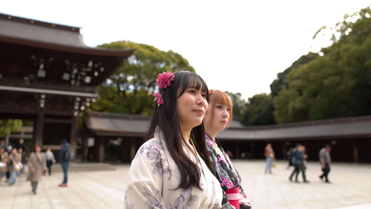 Due donne che indossano kimono tradizionali stanno in un cortile prima di voltare le spalle alla telecamera.