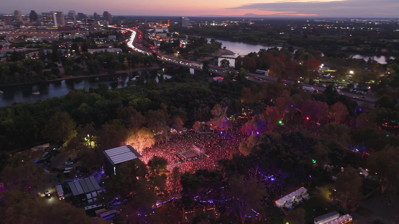 En luftbåren kredsen over Discovery Park i Sacramento under Aftershock Musikfestival, der viser den livlige menneskemængde og festivalopsætningen fra oven