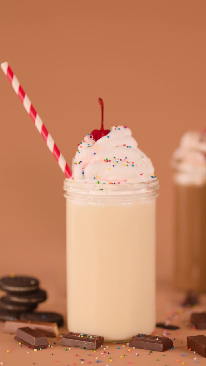 Camera slides from vanilla to chocolate milkshake with whipped cream, cherry, cookies, and sprinkles