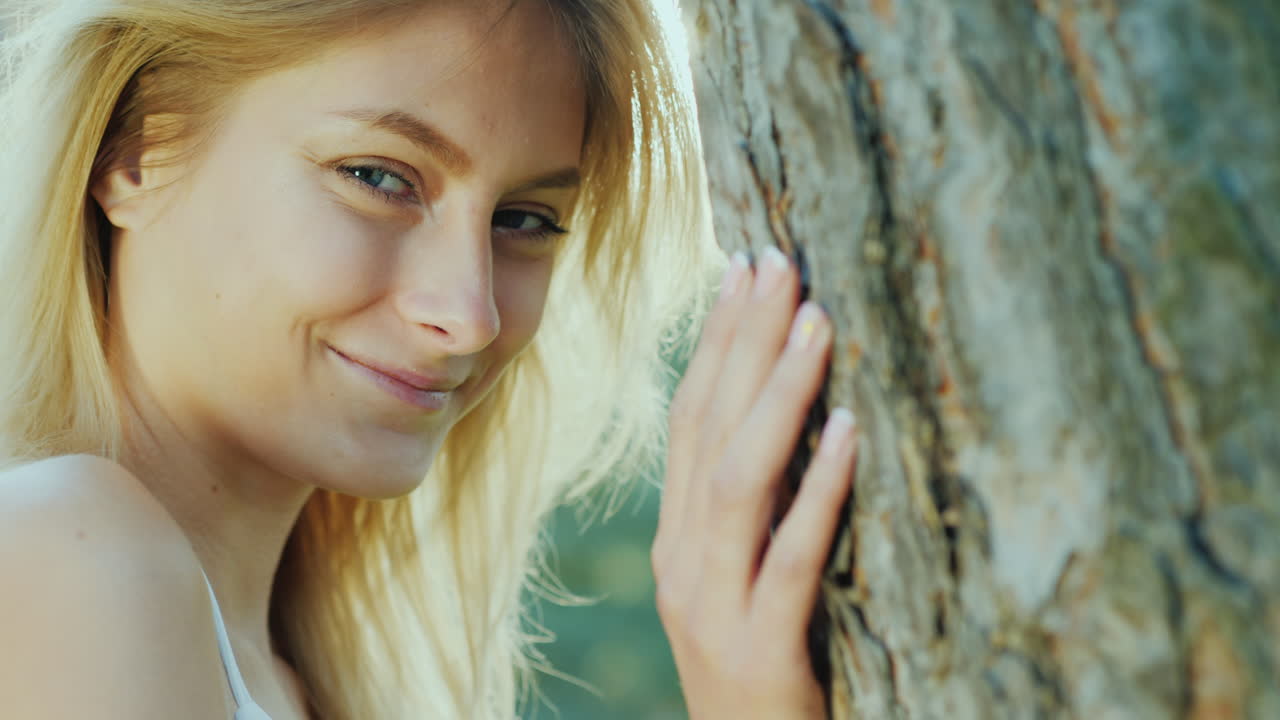 카메라 co를 보고 웃 고 태양에서 나무에 의해 서 있는 아름 다운 젊은 여자의 초상화