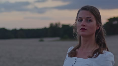 attractive young woman standing in sand dunes at golden hour and looking around