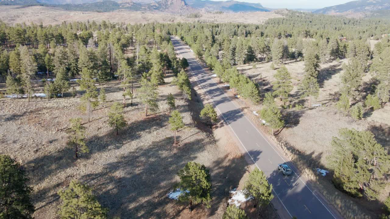 Aerial drone view of the Pike National Forest and a vehicle driving along a remote highway. Forward dolly movement tracking the vehicle. Filmed in the Rocky Mountains of Colorado.