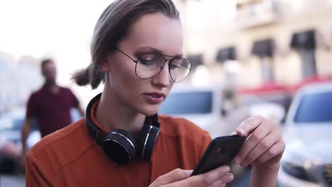 Blondes-Hübsches-Mädchen-Mit-Make-up,-Das-Auf-Der-Straße-Steht-Und-Auf-Ihrem-Schwarzen-Handy-Tippt