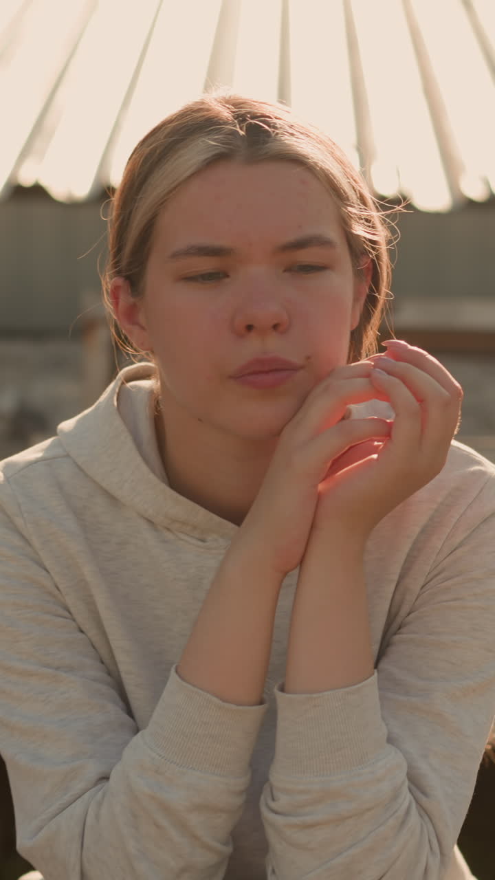 Close-up of a thoughtful woman in casual attire sitting on rustic stadium bleachers, hands joined together, her expression reflects deep contemplation