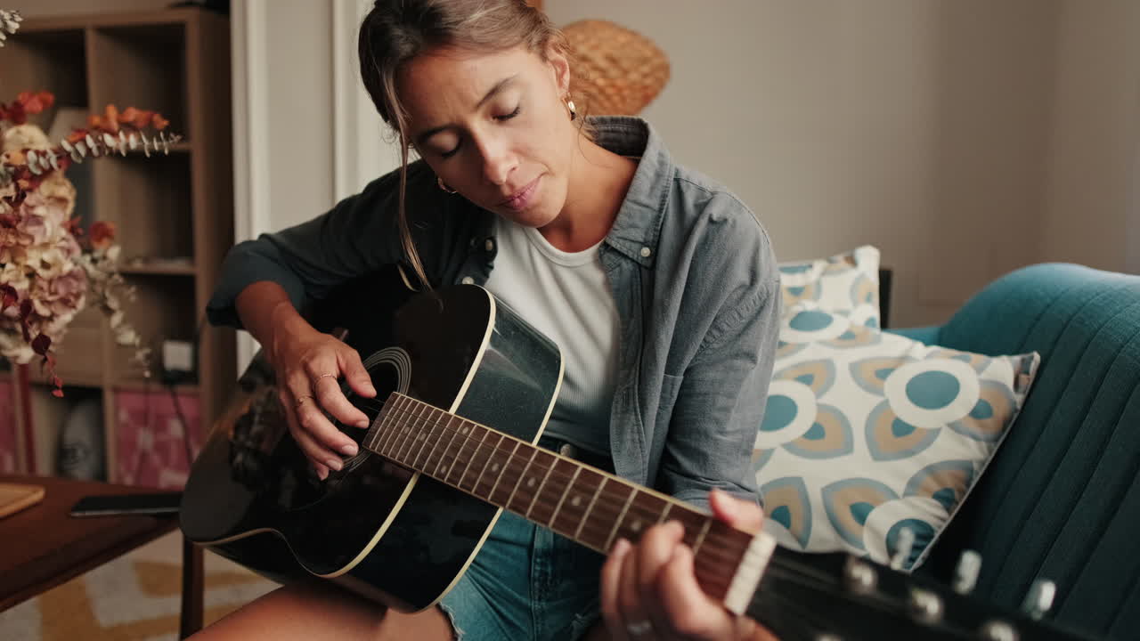 Ung kvinde spiller akustisk guitar derhjemme