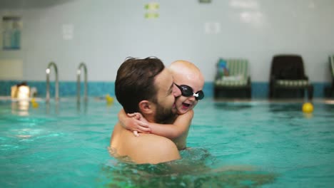 young father lifting his little boy in protective glasses from the water while teaching him how to swim in the swimming pool