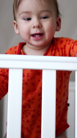 sweet funny little baby standing in white crib. smiling one year old toddler throwing his pacifier happily and gets it back. vertical video