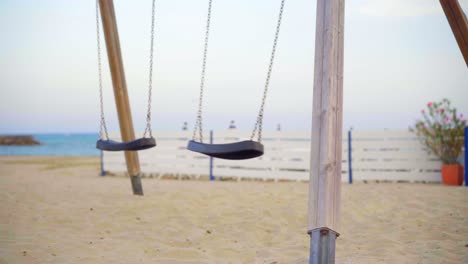 swing slowly swinging in a playground on an sand beach by a blue sea, empty pandemic scene