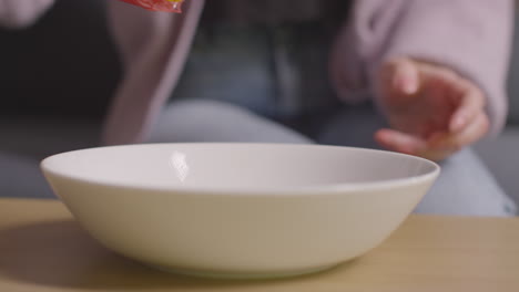 vue rapprochée d'une femme à la maison versant de la tortilla ou des chips de maïs d'un paquet dans un bol sur la table 2