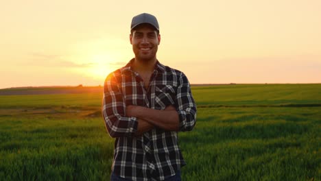 portrait of the handsome young man farmer standing in the field at sunset, smiling to the camera and crossing his hands. high quality 4k footage