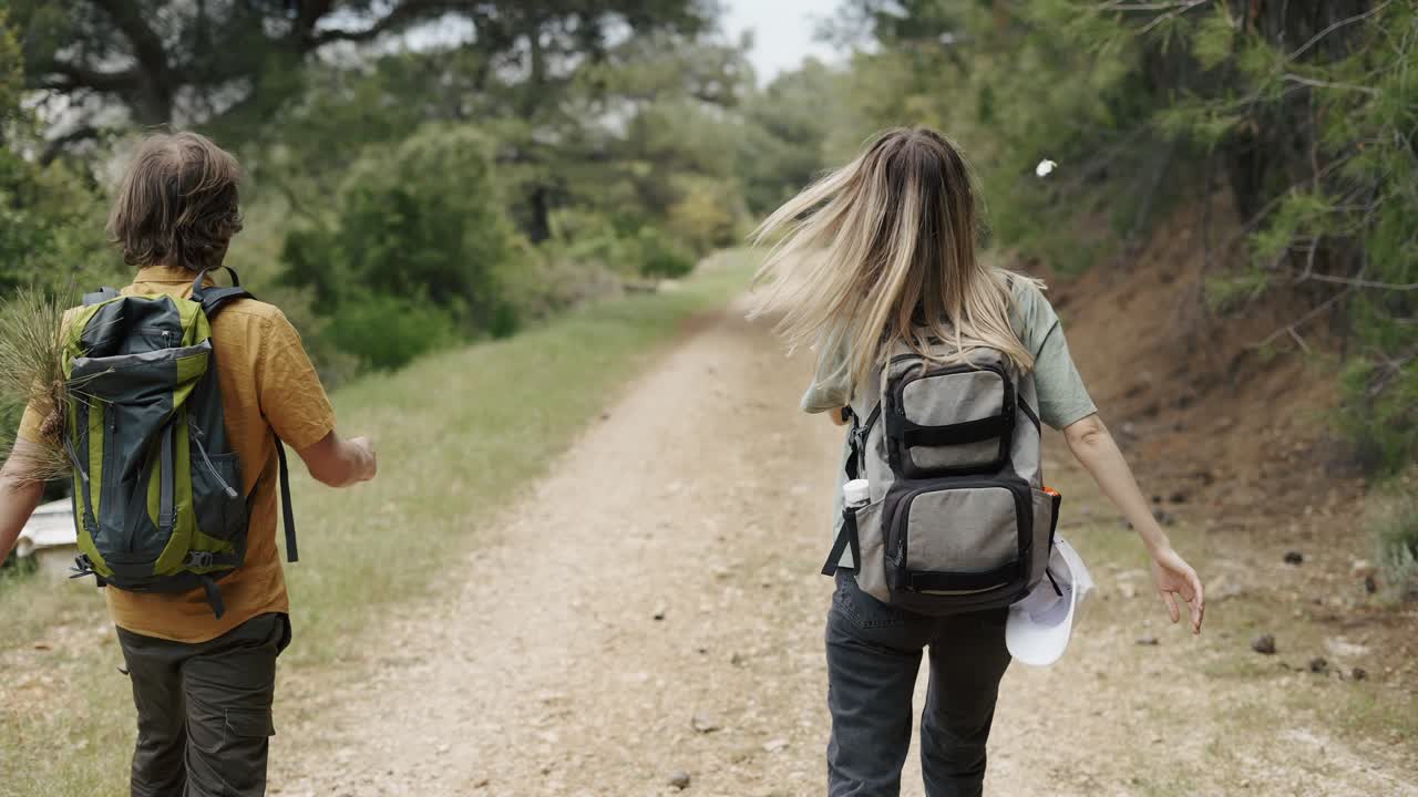 Ein glückliches Rucksacktouristenpaar spaziert auf einem Waldweg und unterhält sich, Rückansicht.
