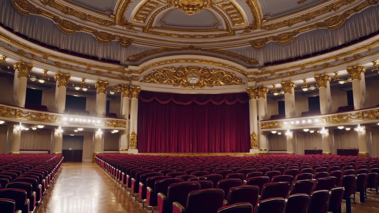 Opulent theater interior with red seats and ornate gold details, captured from a central wide-angle