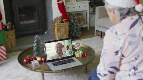 mujer mayor caucásica con sombrero de santa usando una computadora portátil para una videollamada de navidad con un hombre en la pantalla