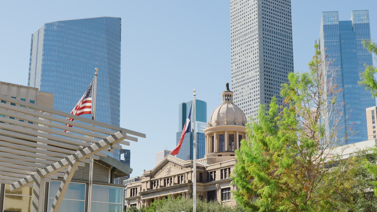 Texas- og amerikanske flag vajer foran Houston Rådhus med Downtown Houstons skyline og moderne skyskrabere i baggrunden på en solskinsdag i Houston, Texas, USA.