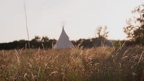 evening shot of mature friends sitting outside teepee as they camp in countryside field